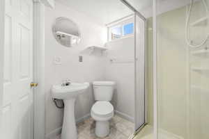 Pedestal sink with chrome faucet, toilet, and glass-enclosed shower