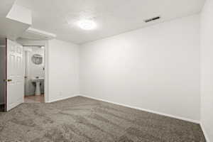 Carpeted room featuring white walls, a ceiling-mounted light fixture, and an open doorway leading to a bathroom with a pedestal sink
