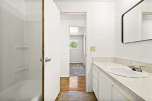 Bathroom featuring a combination bathtub and shower with white surround, a vanity with a drop-in sink, a wall-mounted mirror, and tile-finish flooring