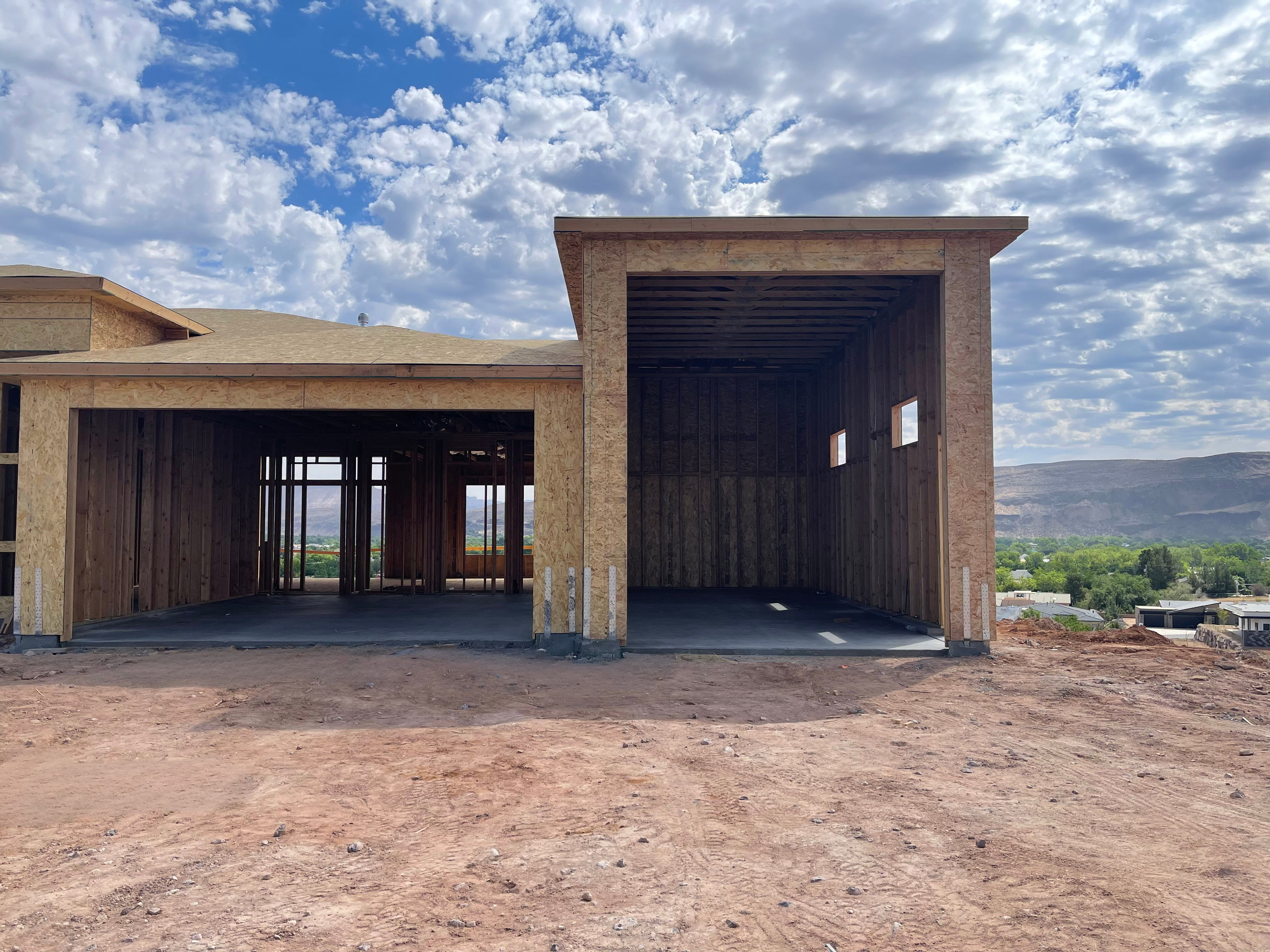 New construction framing with a partial concrete slab, exposed wood sheathing, and a shingled roof