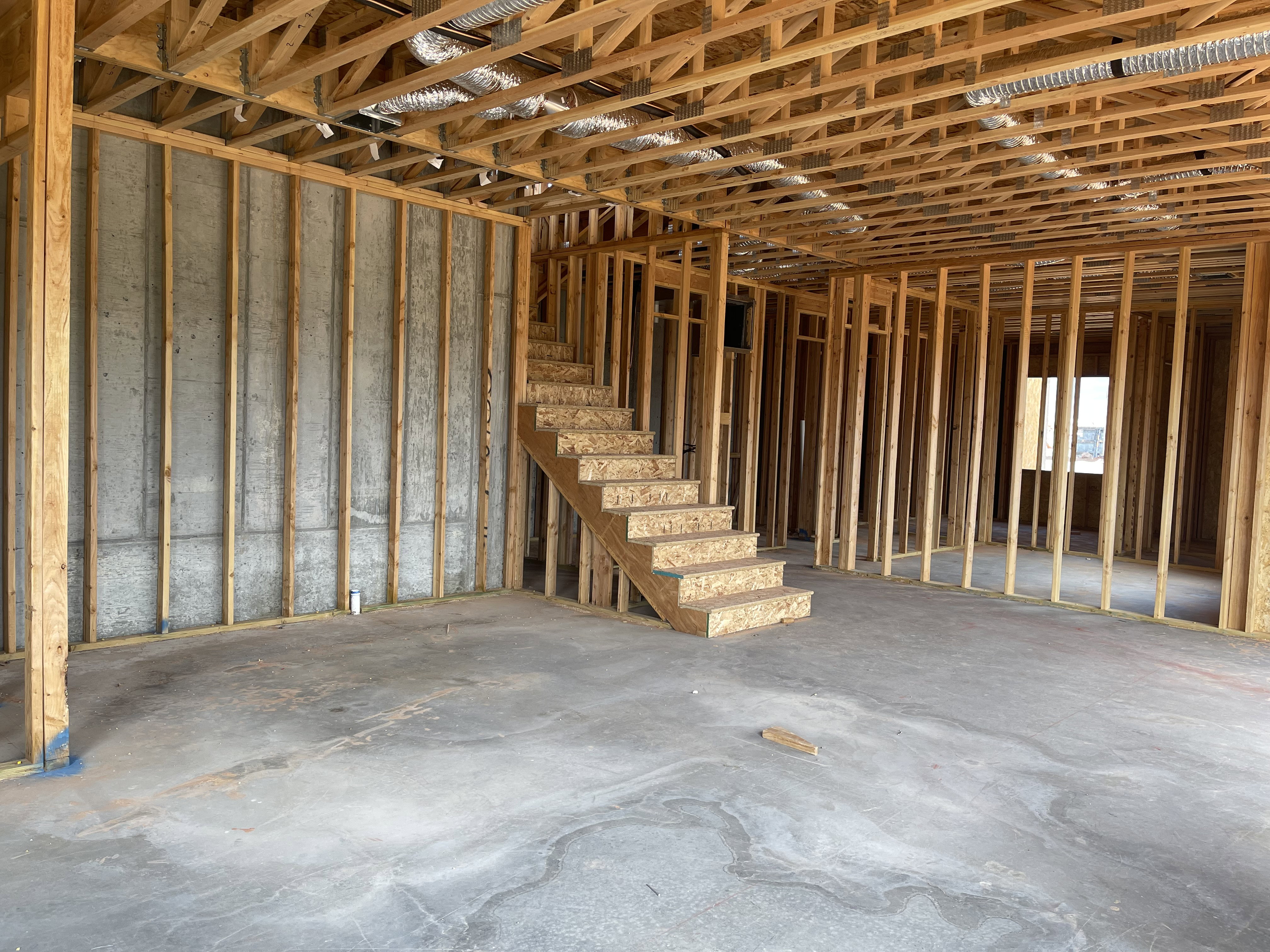 Unfinished interior space featuring exposed wood framing, a concrete slab floor, and an unfinished staircase