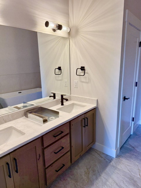 Double vanity with quartz countertops, undermount sinks, and wood-finish cabinetry featuring matte black hardware