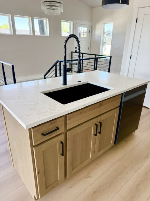 Kitchen island featuring a black composite sink, matte black pull-down faucet, and light wood cabinetry with black hardware