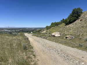 Gravel pathway traversing a natural hillside, featuring distant urban scenery and a clear blue sky
