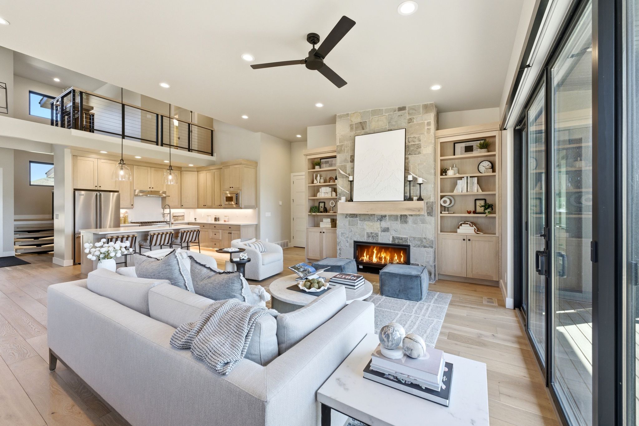 Spacious living area featuring light wood-finish flooring, a stacked stone fireplace with a natural wood mantel, and built-in shelving