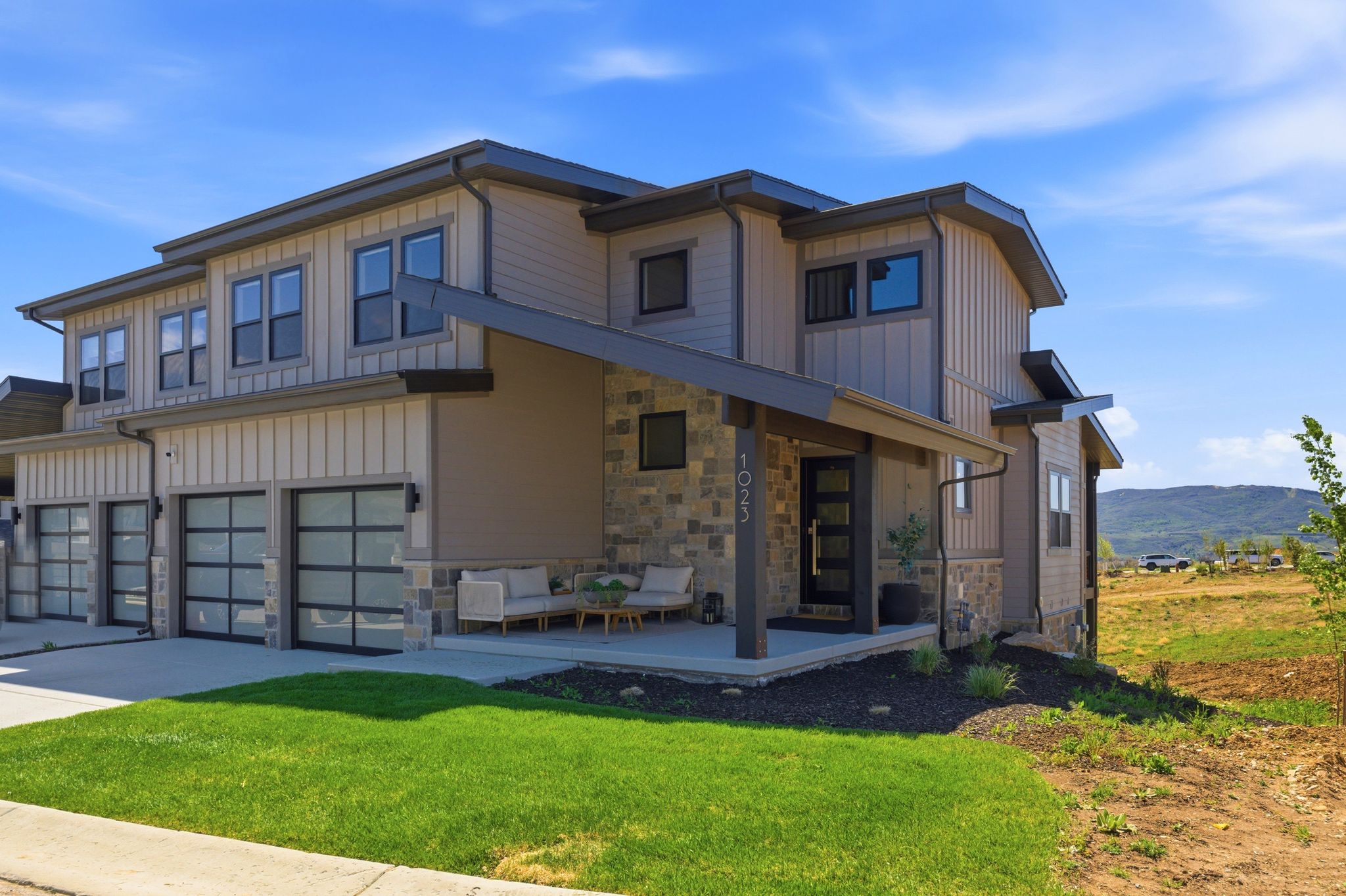 Contemporary multi-level exterior featuring tan siding, stone accents, and dark trim