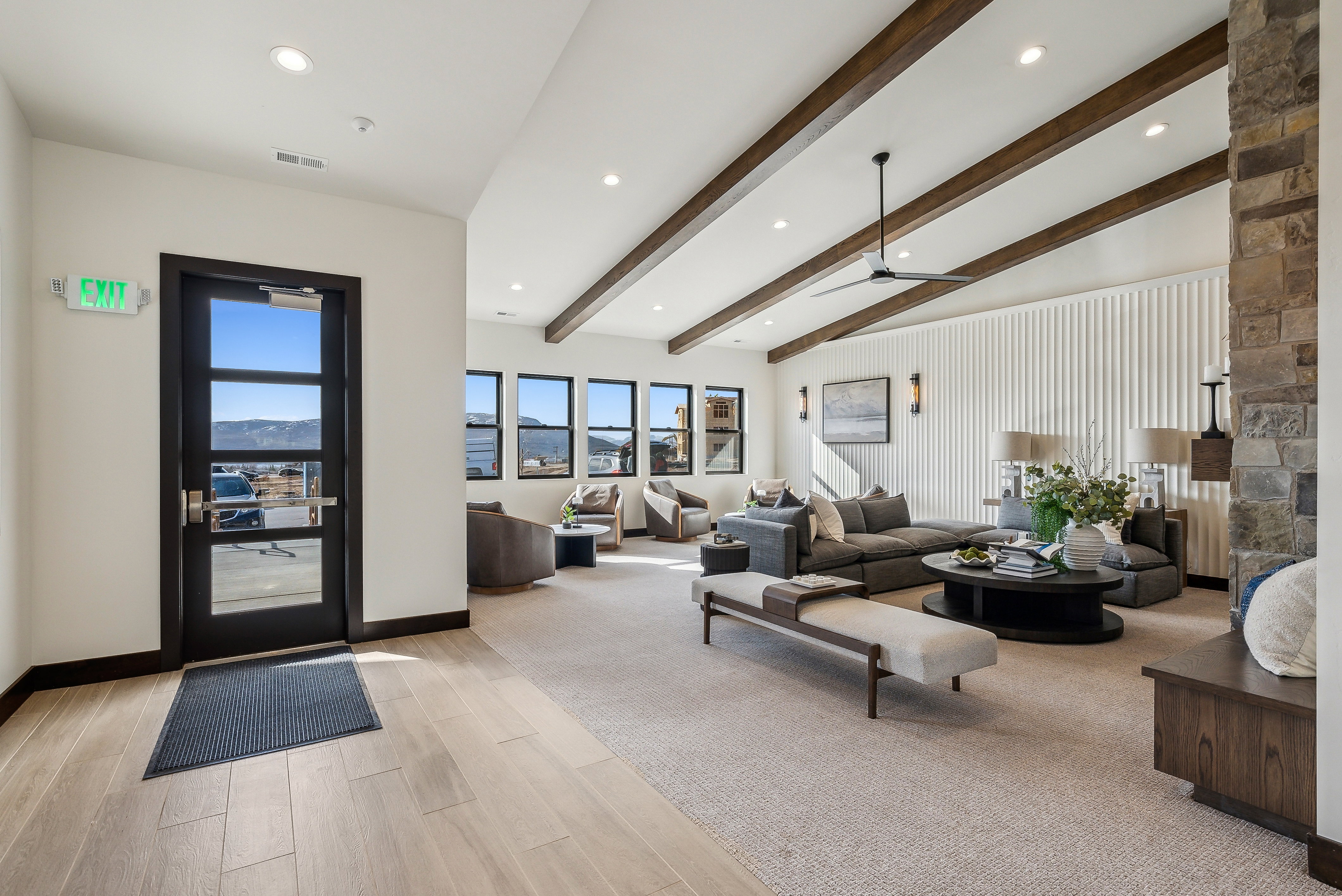 Spacious living area featuring wood-finish flooring, a vaulted ceiling with exposed beams, recessed lighting, and a stone-clad fireplace