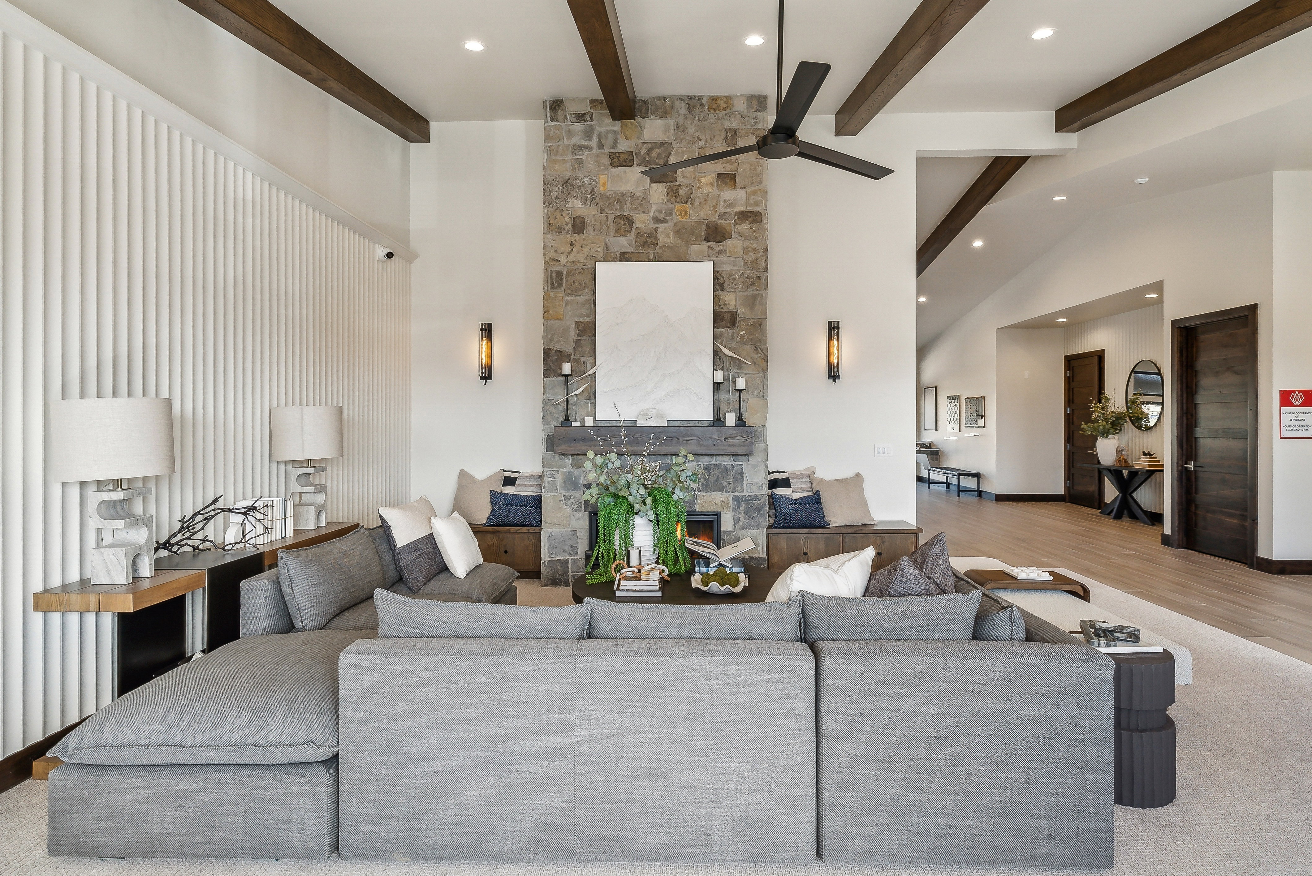 Spacious interior featuring a stone-clad fireplace, built-in bench seating, exposed wood ceiling beams, and a modern ceiling fan