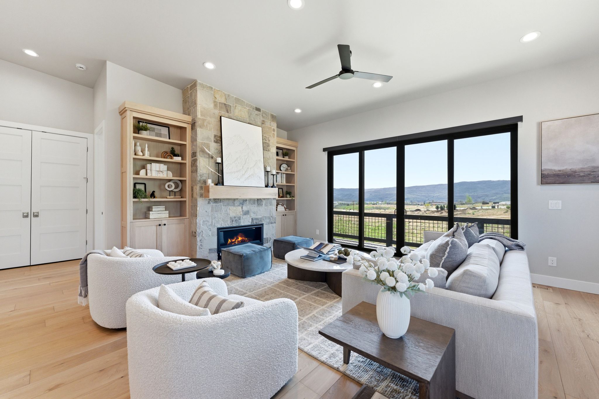 Spacious living area featuring a stone fireplace with a wood mantle, built-in shelving, hardwood flooring, and sliding glass doors opening to a scenic mountain backdrop