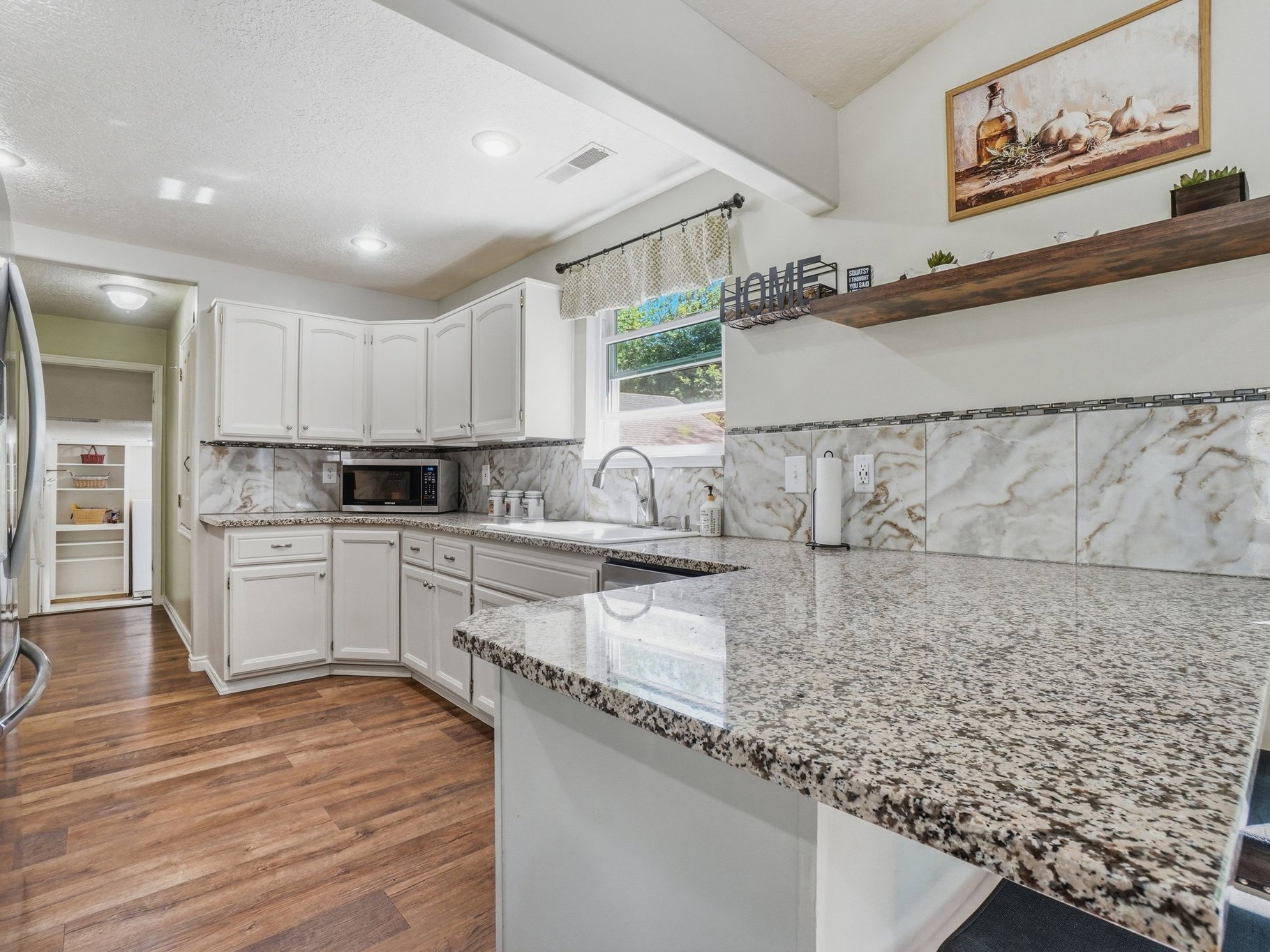 Kitchen featuring white cabinetry, granite countertops, tile backsplash, and wood-finish flooring