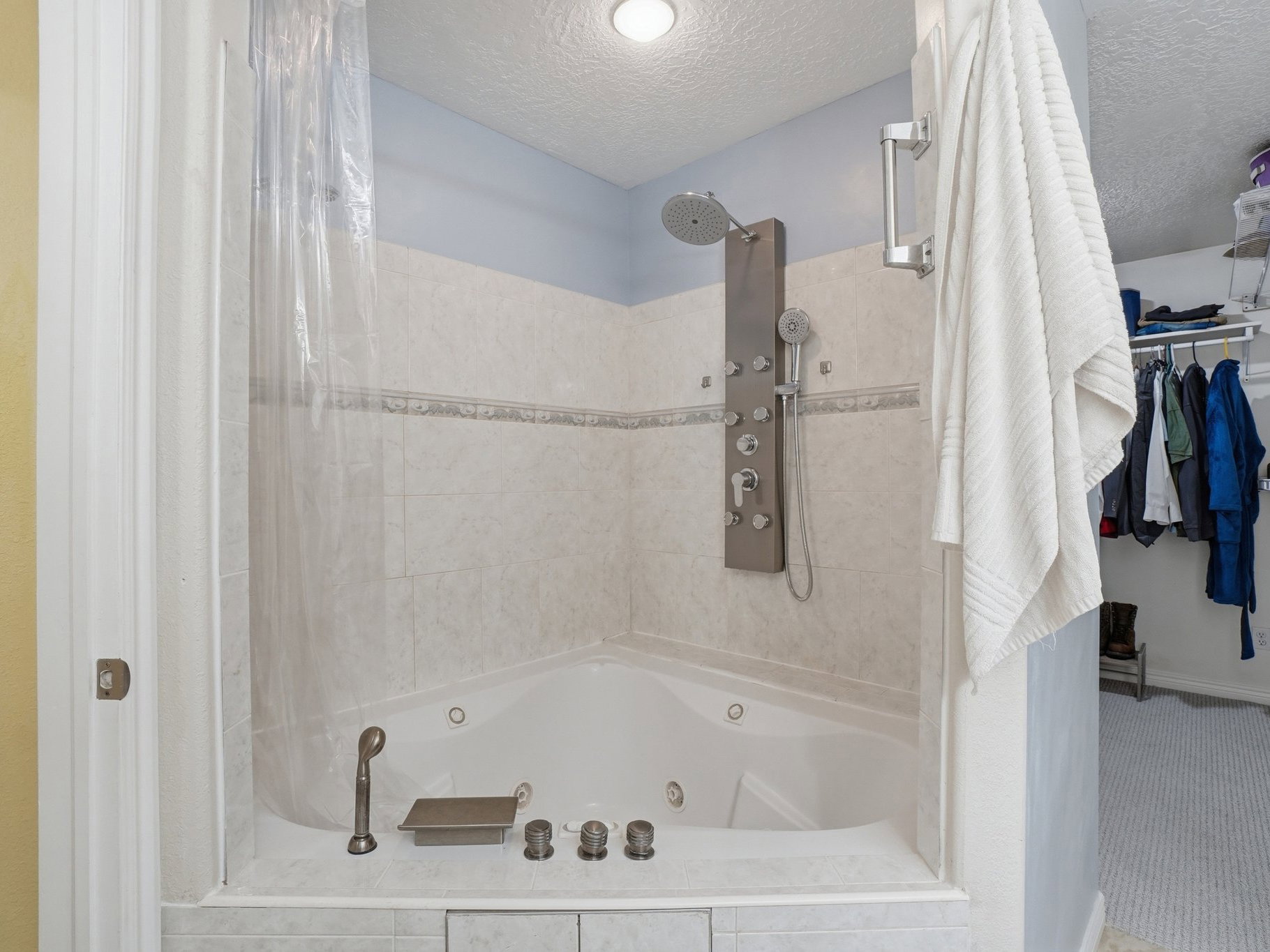 Corner jetted tub with tiled surround, rain shower head, multi-jet shower panel, and handheld shower wand