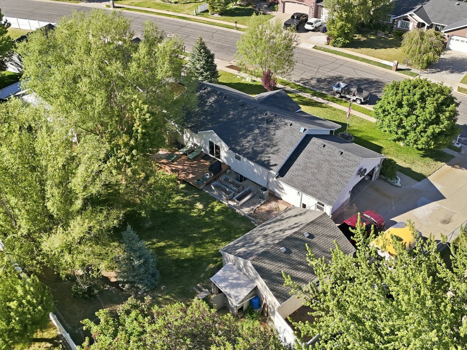 Aerial overview showcasing a residential property with a multi-level deck, mature trees, and a paved driveway