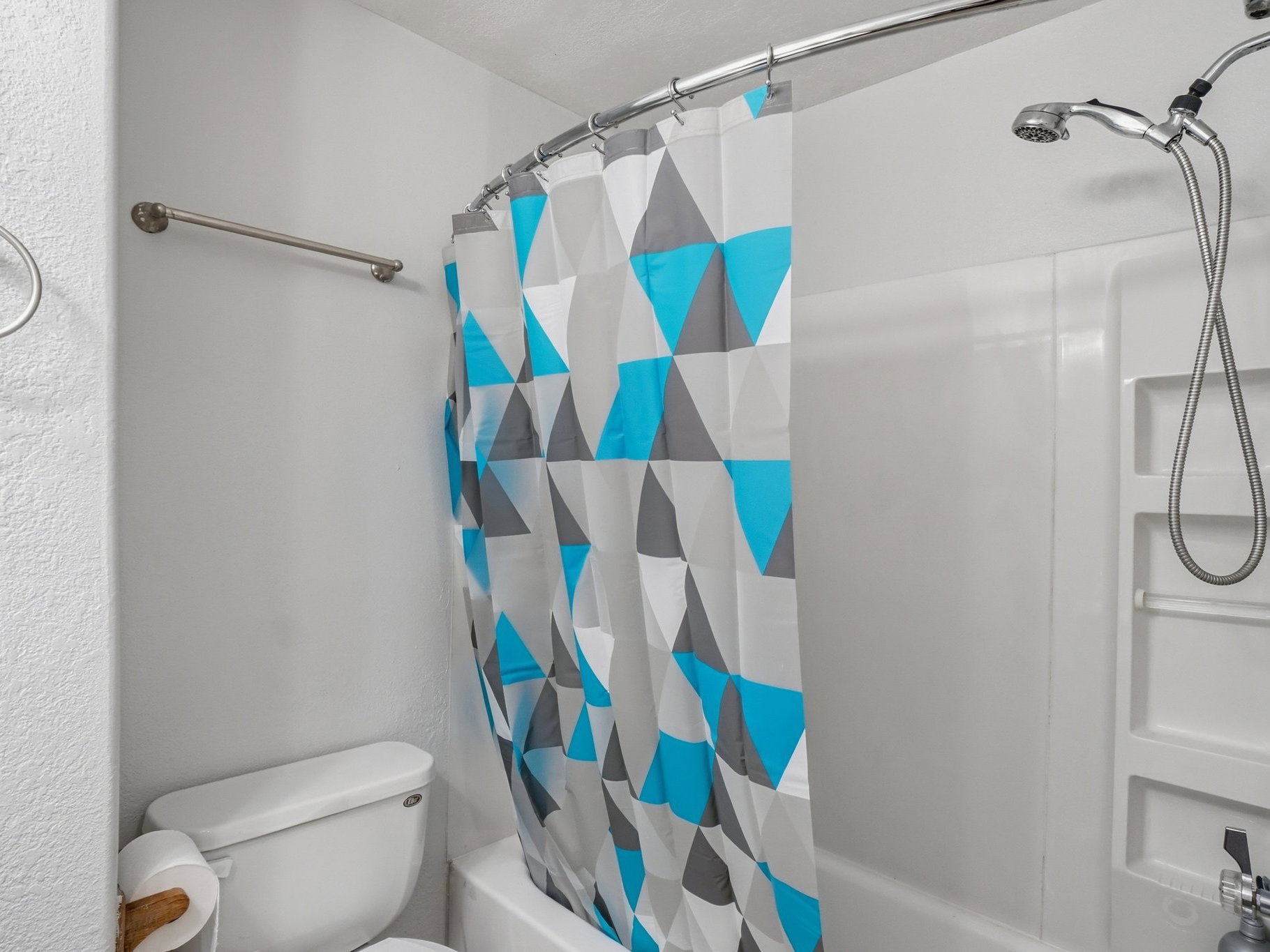 White shower/tub combination featuring an integrated corner shelving unit and a handheld showerhead