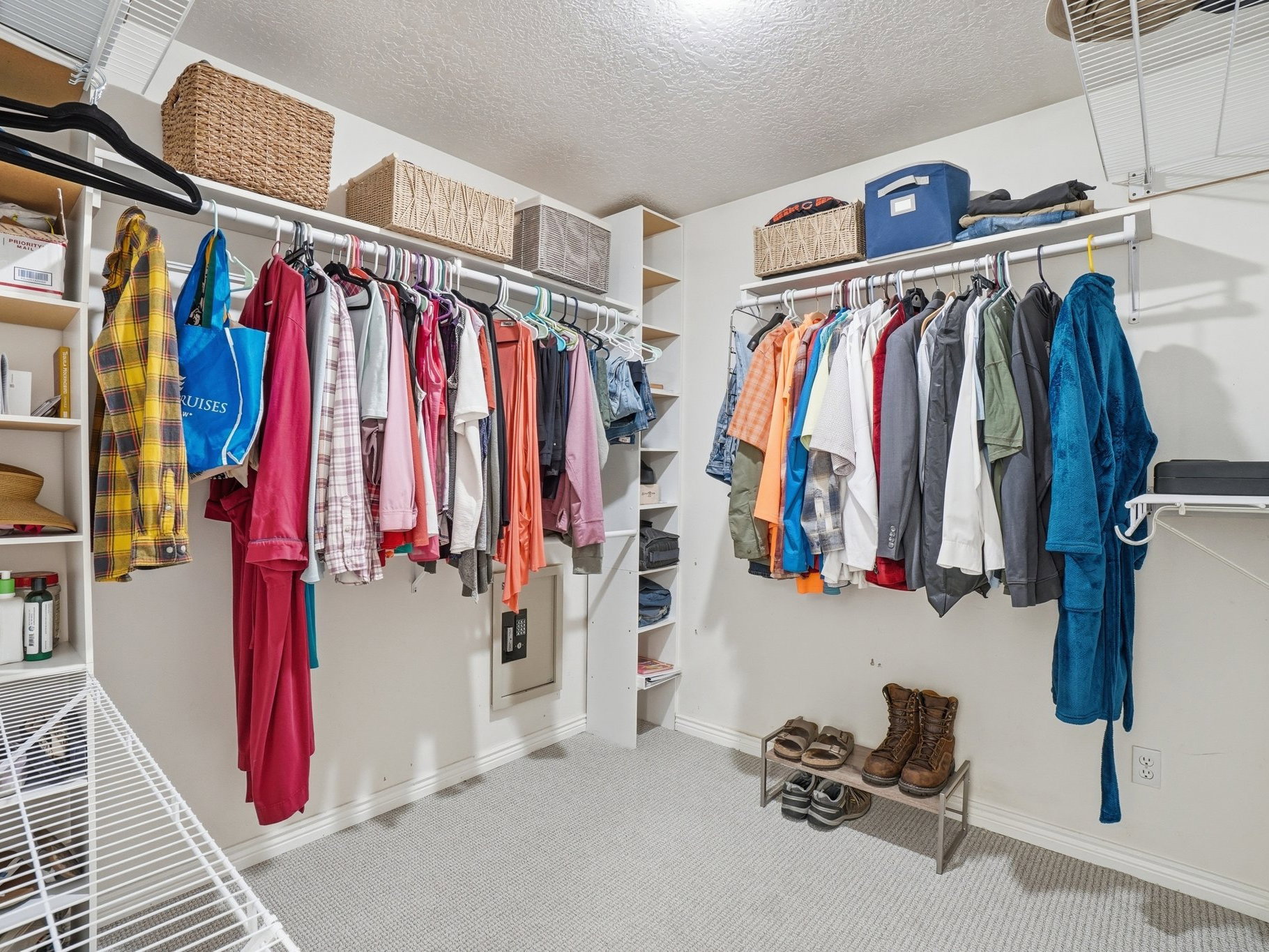 Spacious walk-in closet featuring white wire shelving, multiple hanging rods, built-in wooden shelving, light gray carpet flooring, and white baseboards