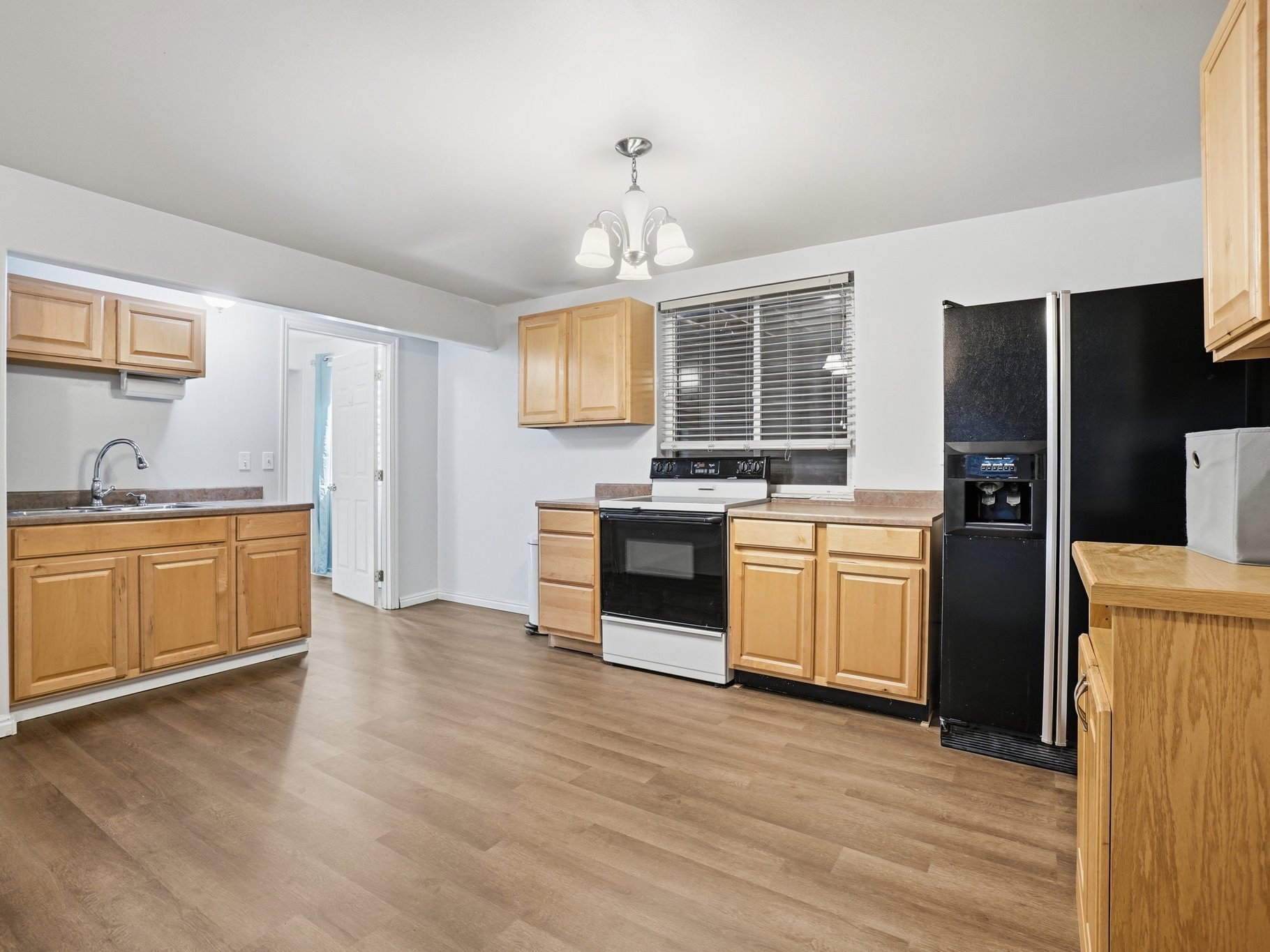 Kitchen featuring wood-finish flooring, light wood cabinetry, laminate countertops, a stainless steel sink with a gooseneck faucet, and integrated black appliances