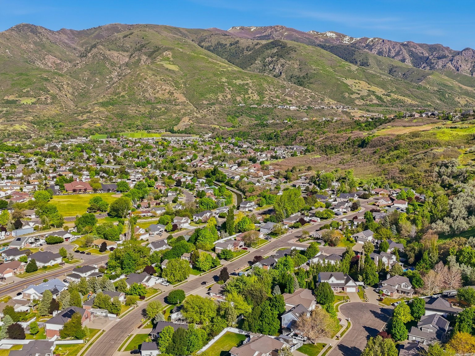 Expansive aerial perspective showcasing a residential community nestled at the base of verdant mountains