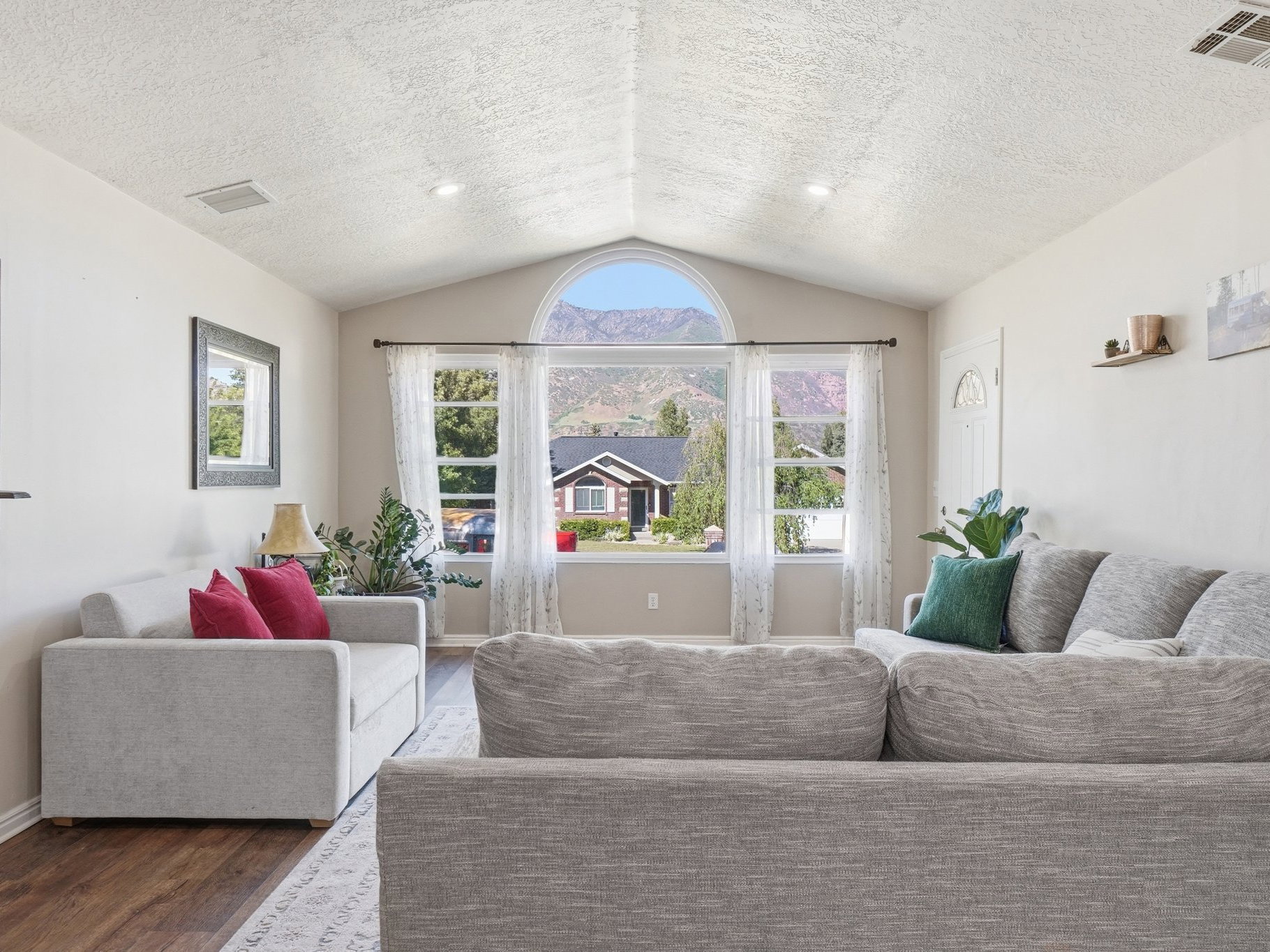 Vaulted ceiling living area featuring wood-finish flooring, a prominent arched window, and recessed lighting