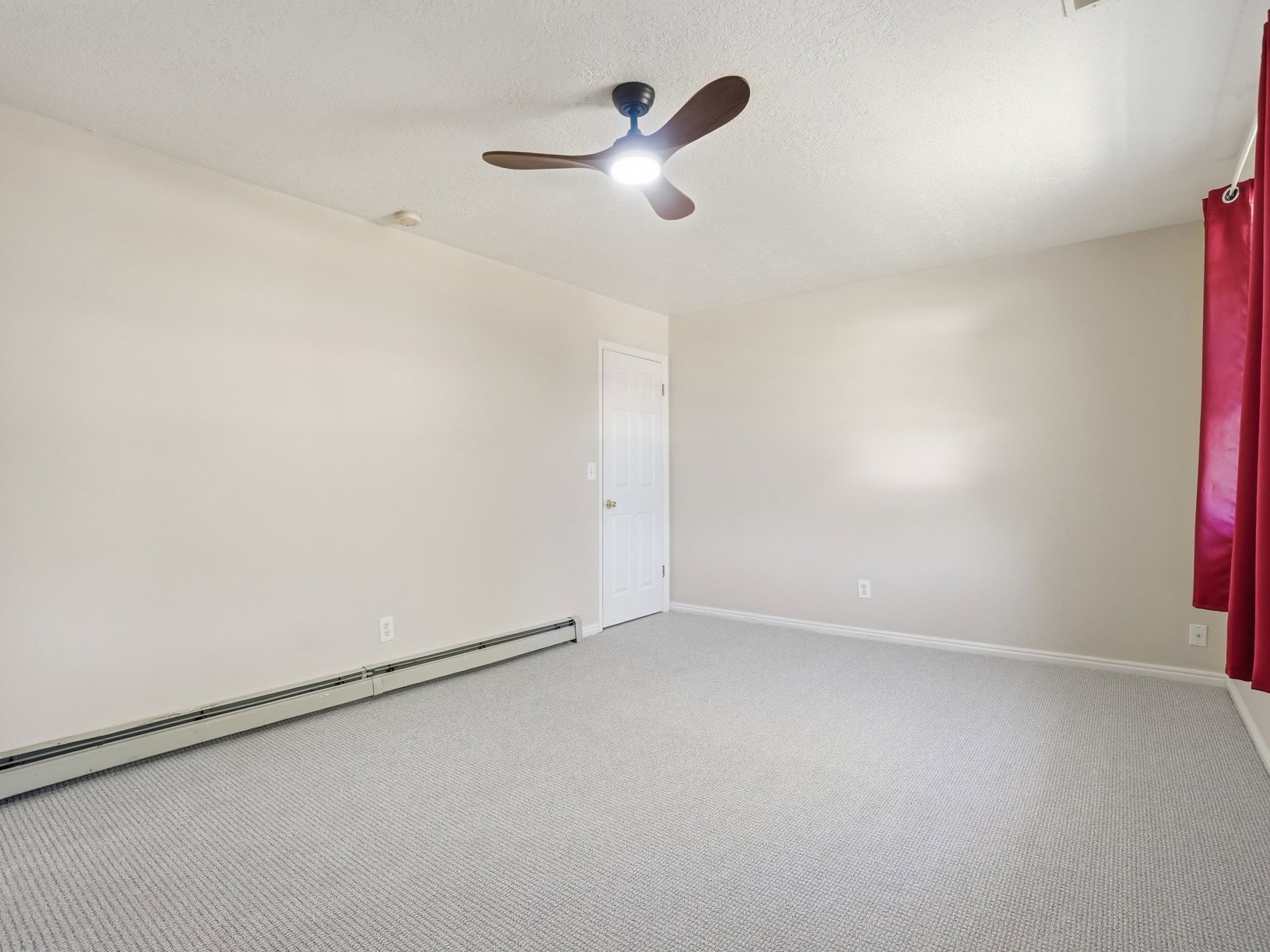 Carpeted room with a ceiling fan, baseboard heating, a white door, and light-colored walls