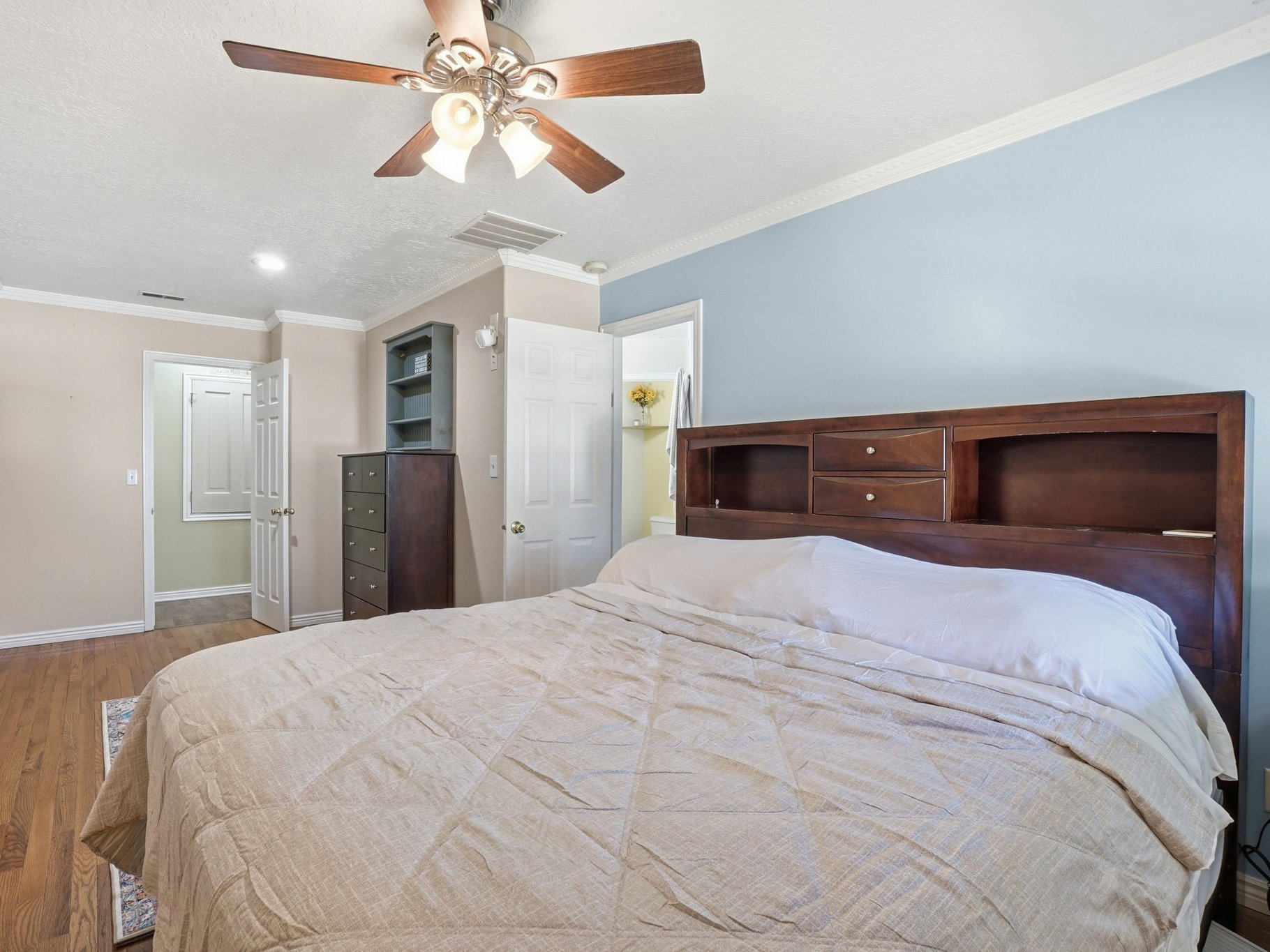 Spacious room featuring wood-finish flooring, a ceiling fan with integrated lighting, crown molding, and two-tone wall paint