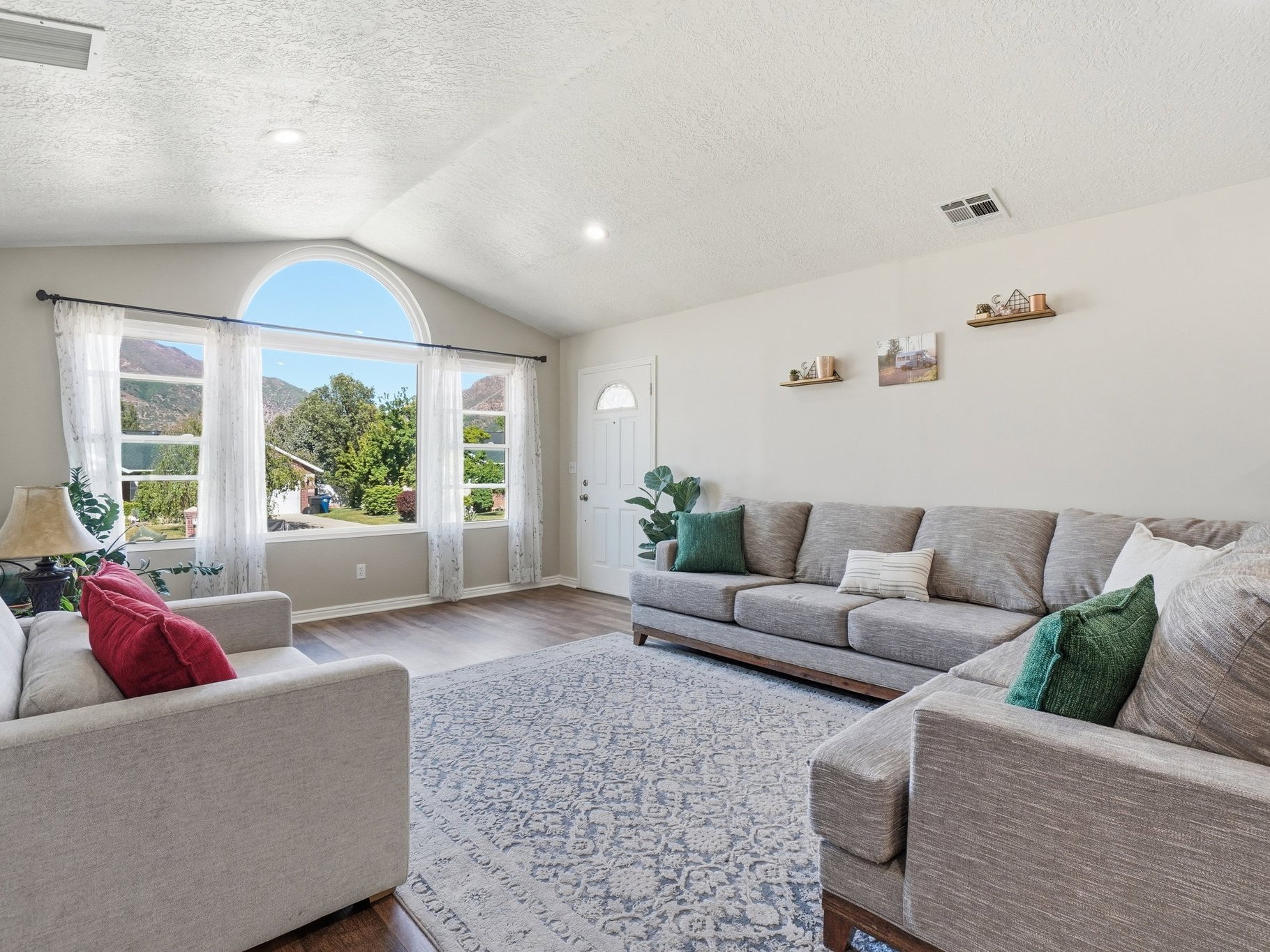 Vaulted ceiling living area featuring a large arched picture window, wood-finish flooring, and recessed lighting