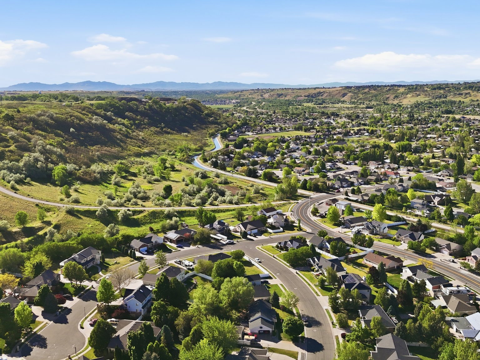 Expansive aerial perspective showcasing a residential development with winding roads and numerous homes, surrounded by natural hillsides and green landscaping