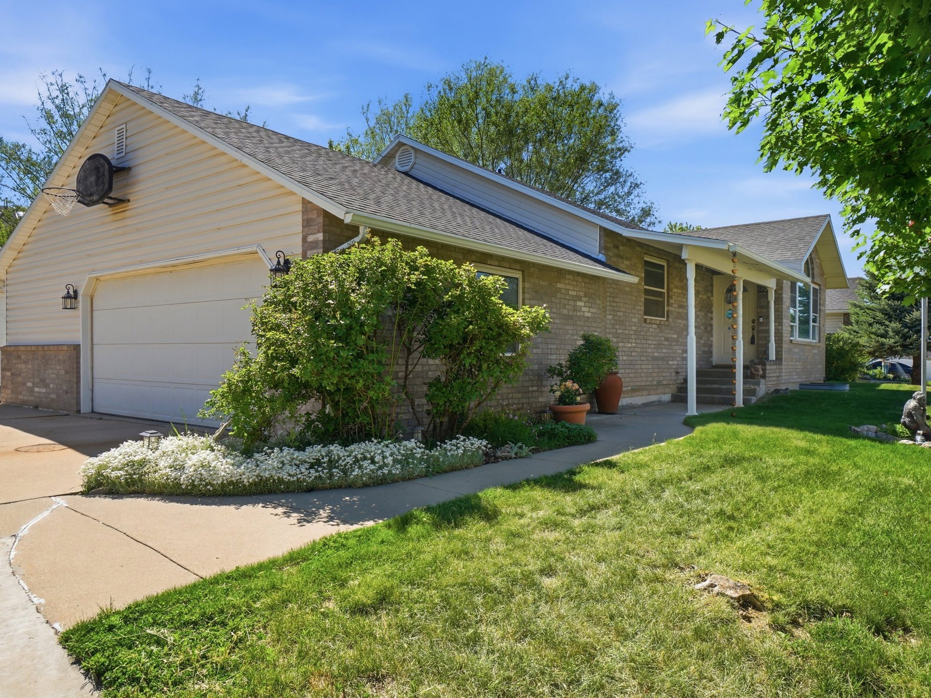 Brick and siding exterior featuring a two-car garage with overhead door, paved driveway, and covered front porch with white columns