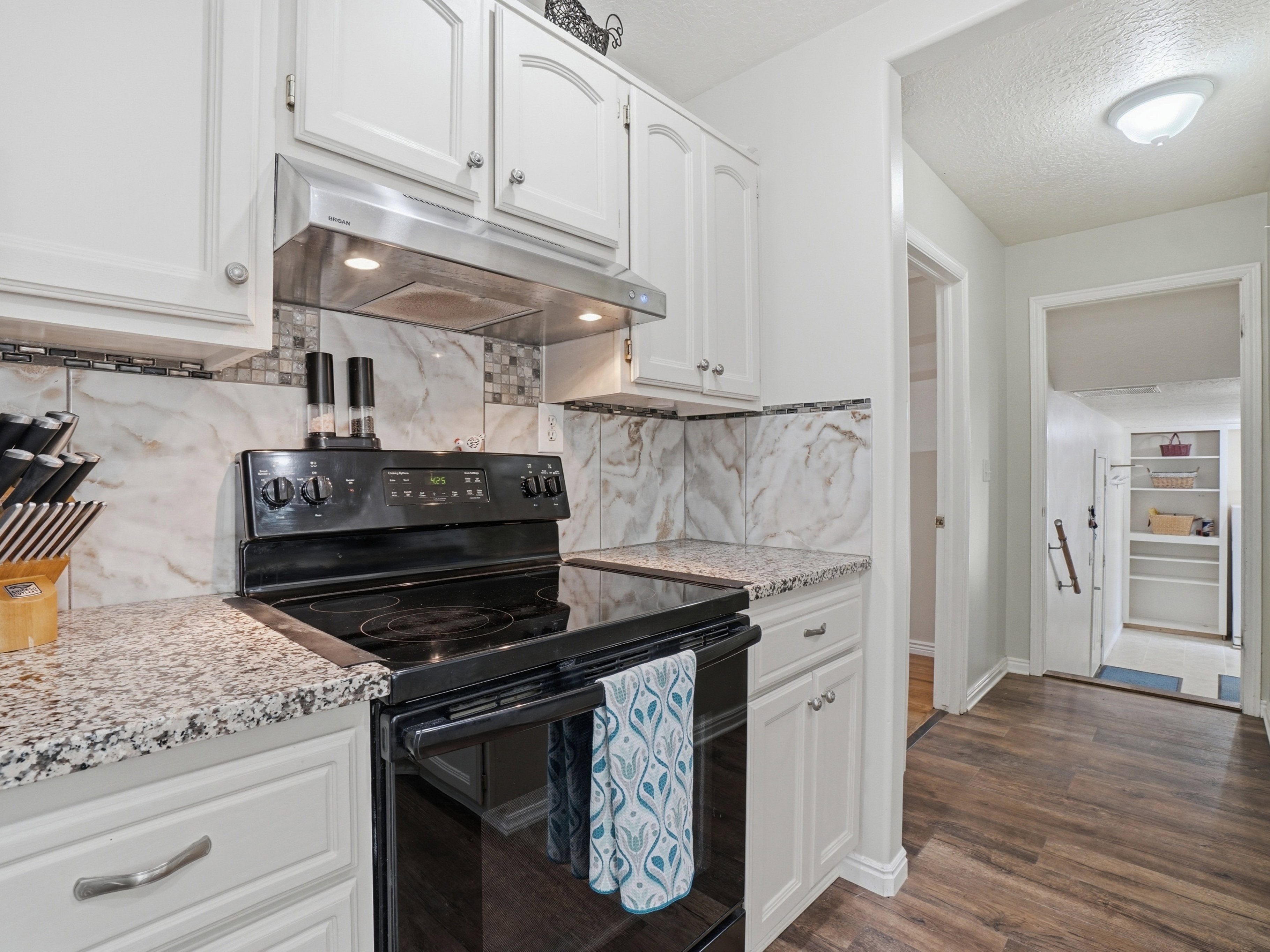 Kitchen featuring white cabinetry, granite-finish countertops, black electric range with a stainless steel vent hood, and a decorative tile backsplash