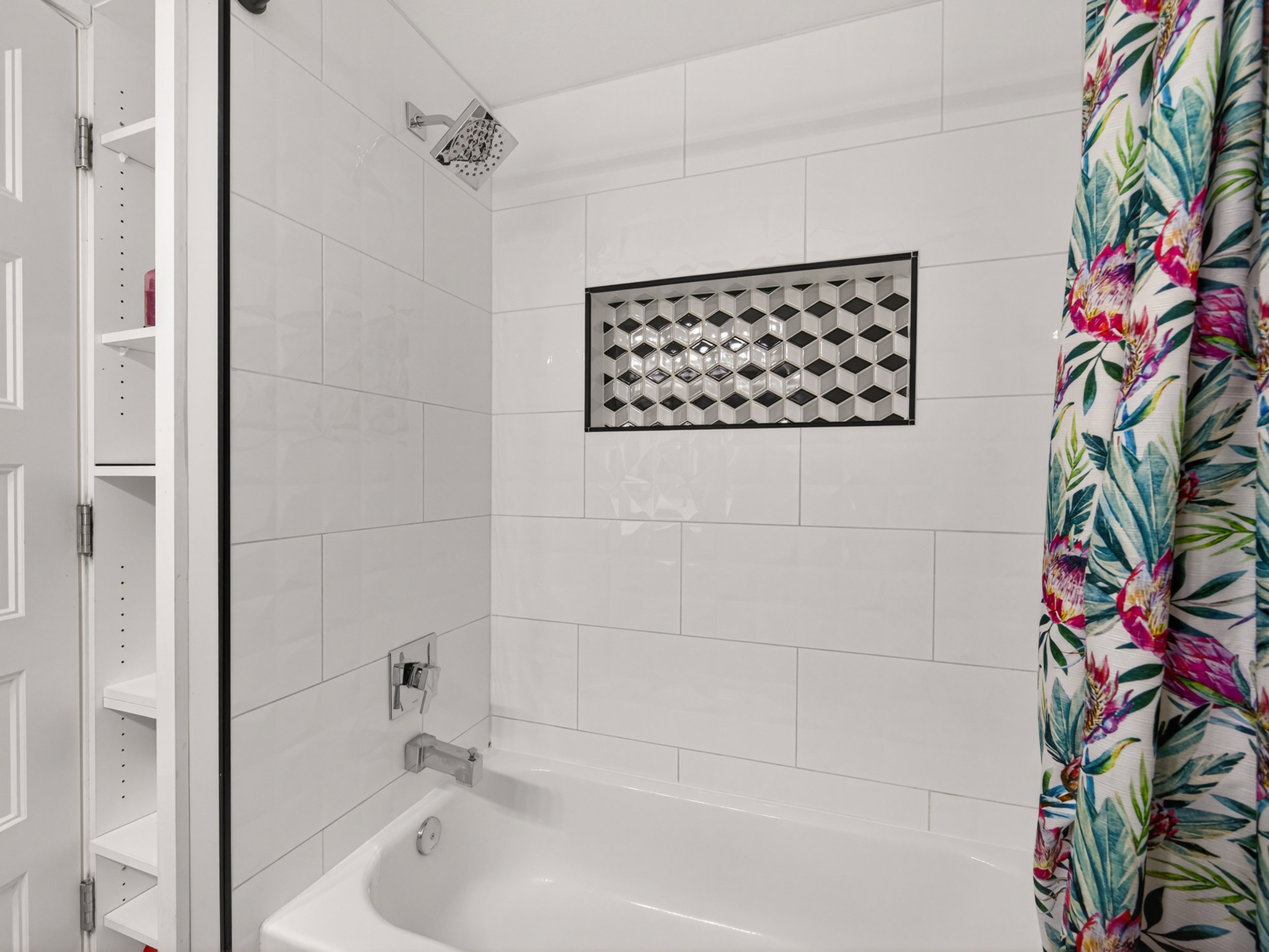 Bathtub with white subway tile surround, featuring a geometric patterned tile niche and a chrome shower head and faucet