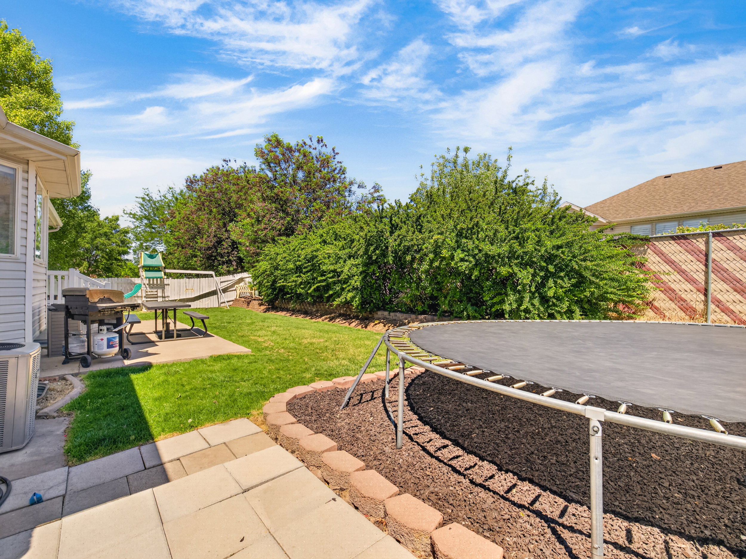 Spacious backyard featuring a manicured lawn, a concrete patio, and mature perimeter landscaping