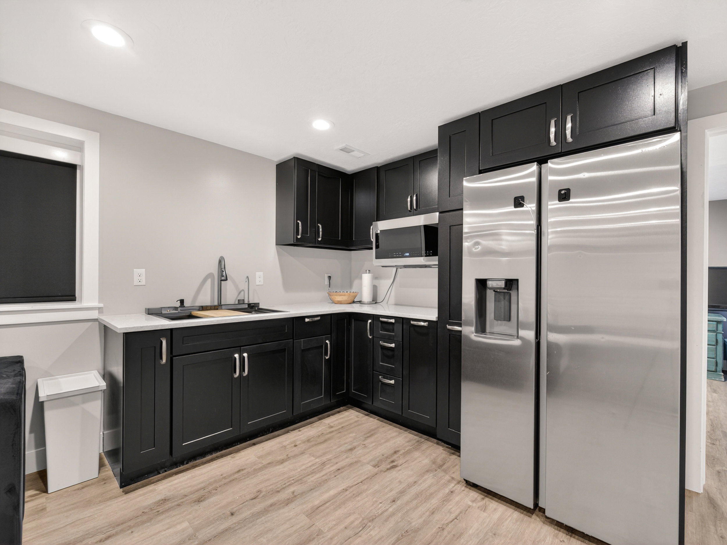 Kitchenette featuring dark cabinetry, light countertops, wood-finish flooring, a stainless steel refrigerator, and a built-in microwave
