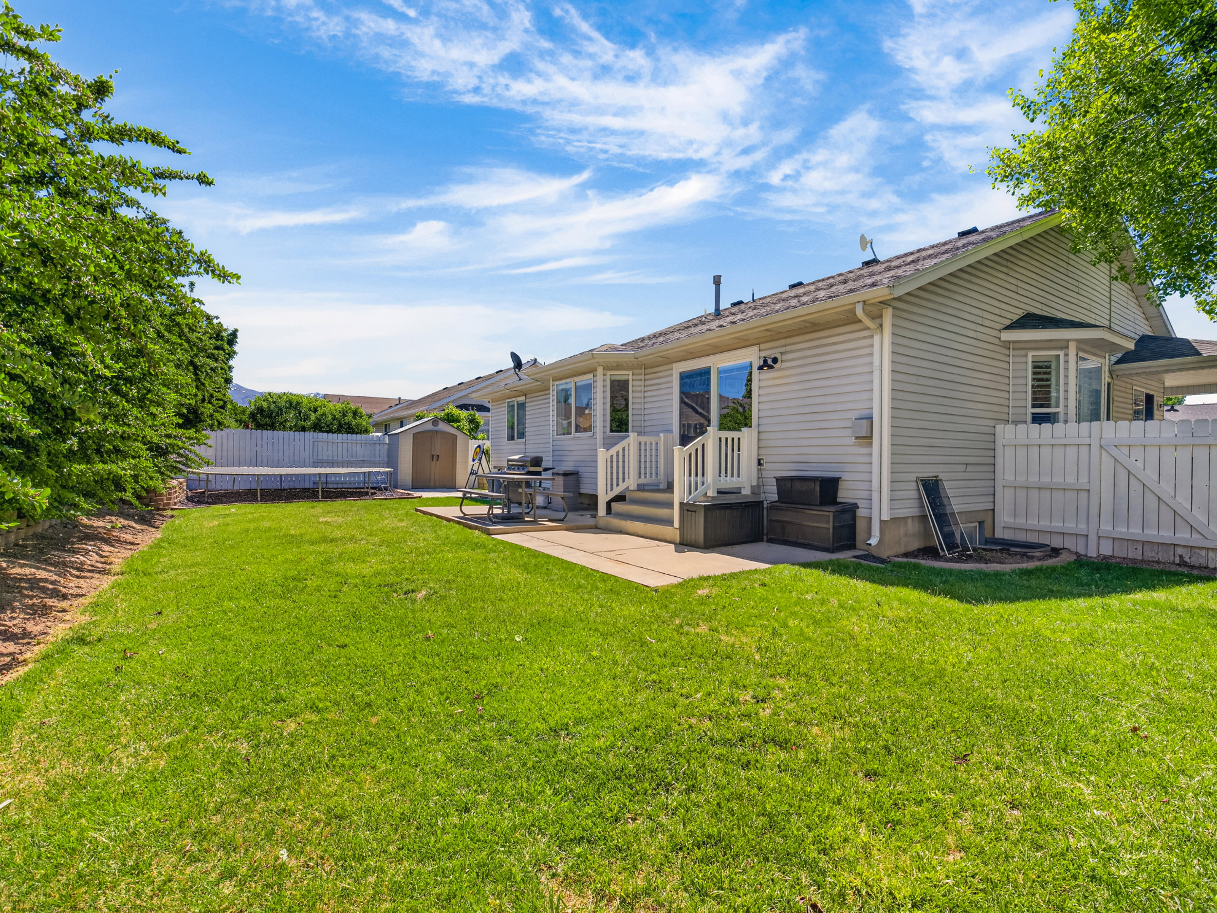 Expansive backyard featuring a manicured lawn, a concrete patio, and a storage shed