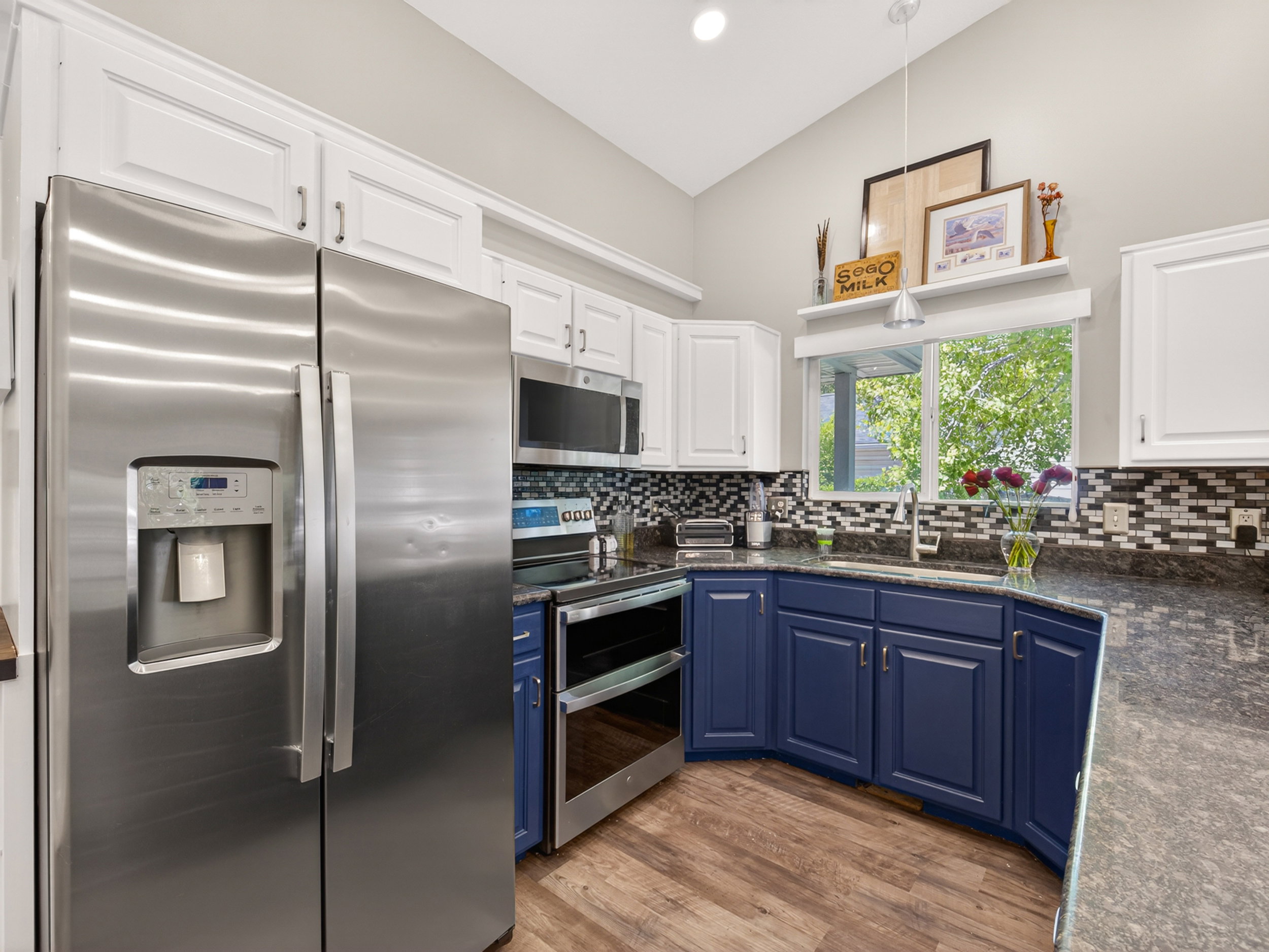 Kitchen featuring a vaulted ceiling with pendant lighting, wood-finish flooring, stainless steel appliances, two-tone cabinetry, and a mosaic tile backsplash