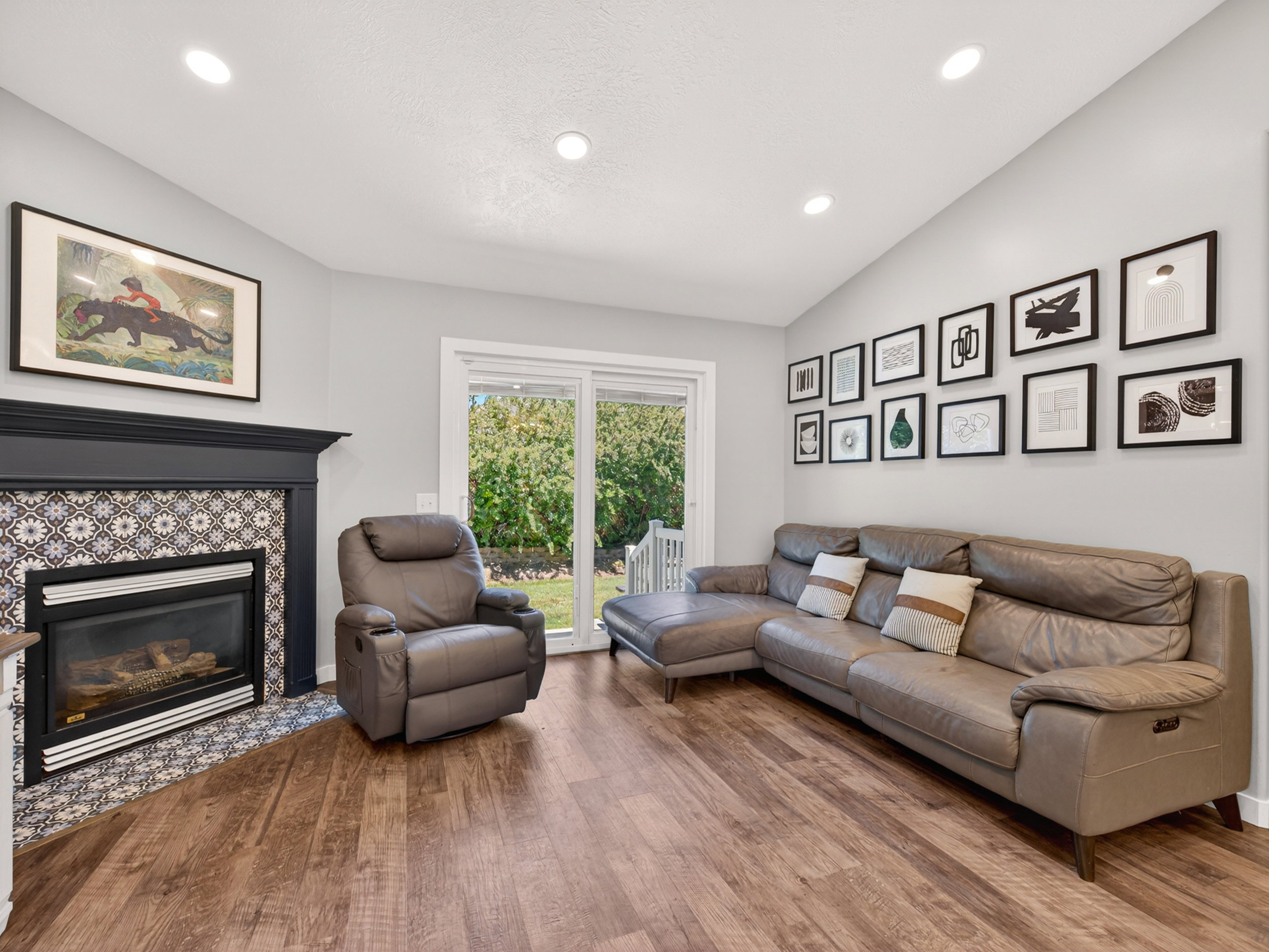 Living area with vaulted ceiling, recessed lighting, wood-finish flooring, a fireplace featuring decorative tile surround and mantel, and sliding glass doors to outdoor space