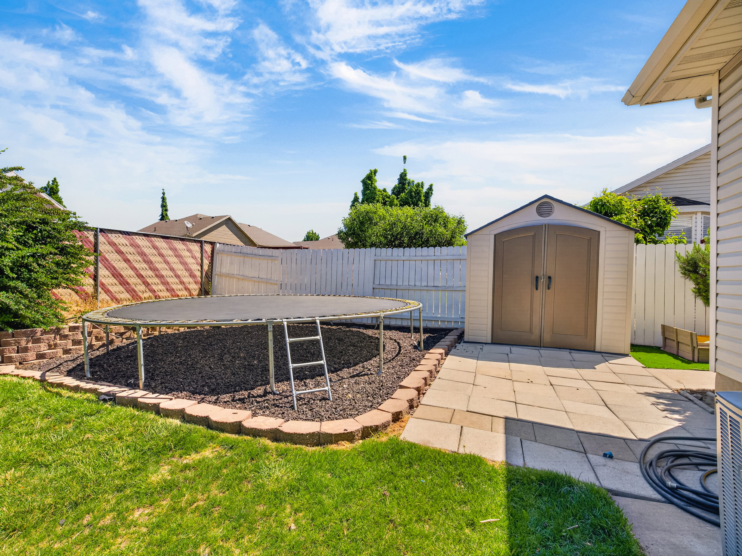 Expansive backyard featuring a green lawn, a privacy fence, a multi-paneled storage shed, and a stone paver patio