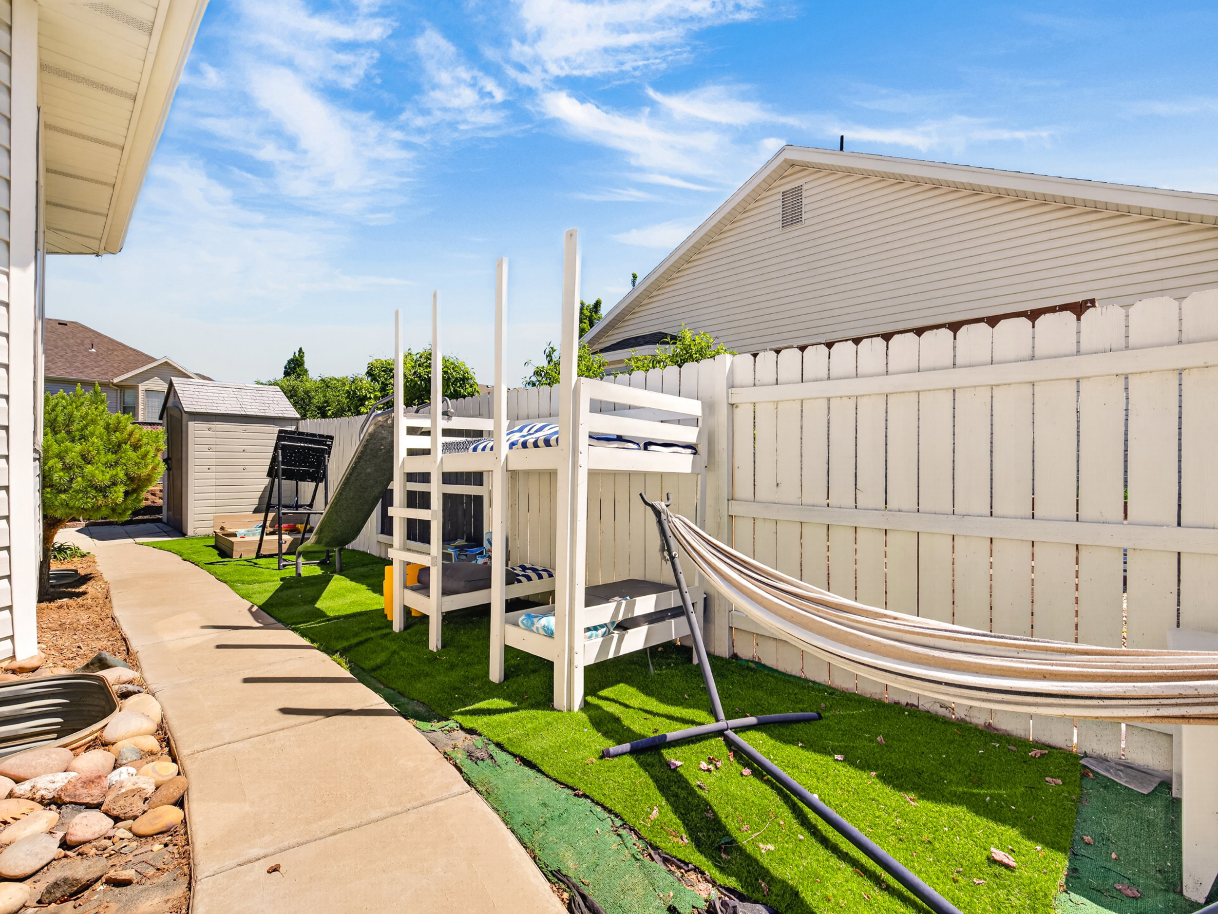 Side yard featuring a concrete pathway, artificial turf, and a white picket fence