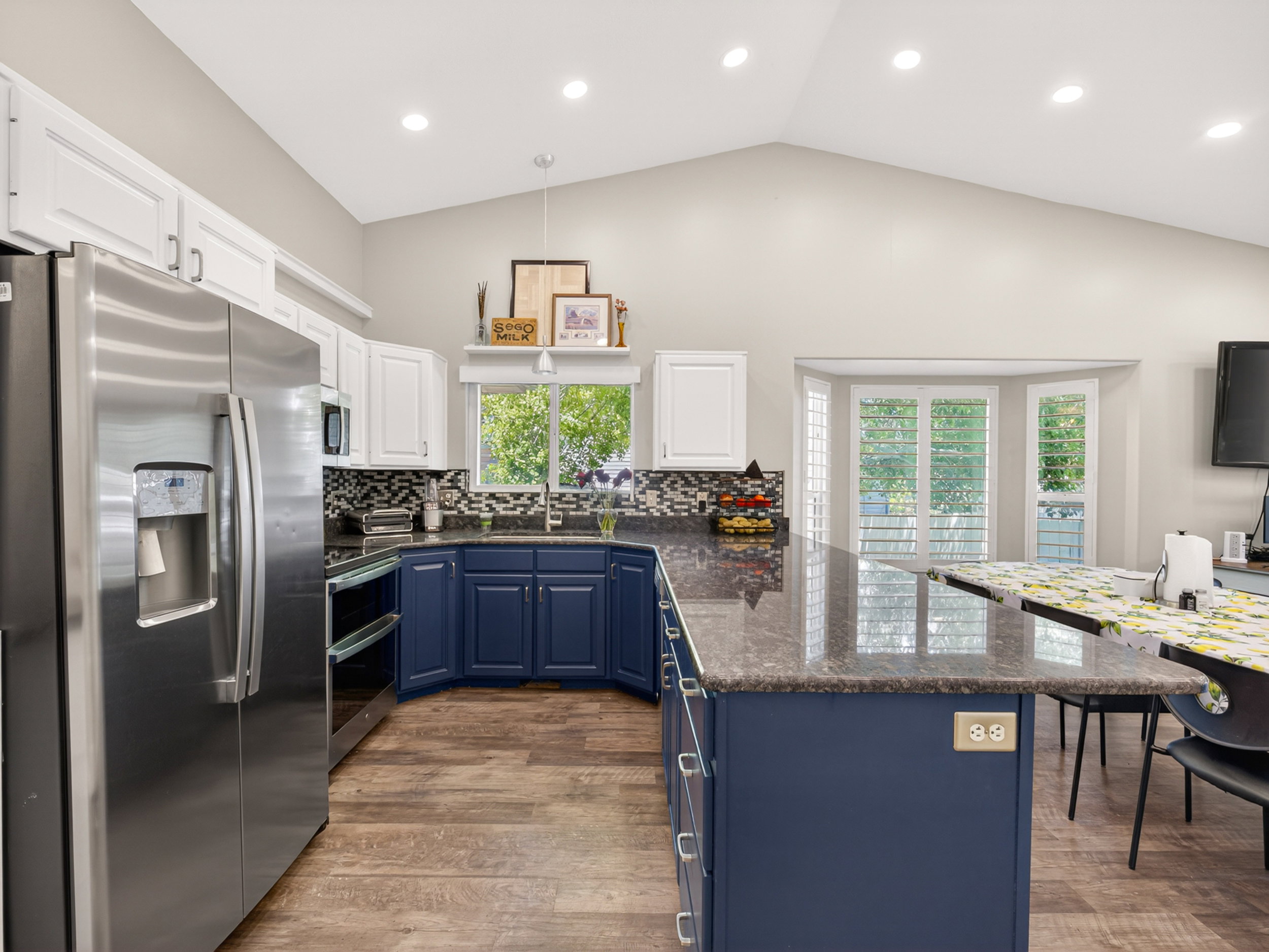 Vaulted ceiling kitchen featuring wood-finish flooring and a large island with stone countertops