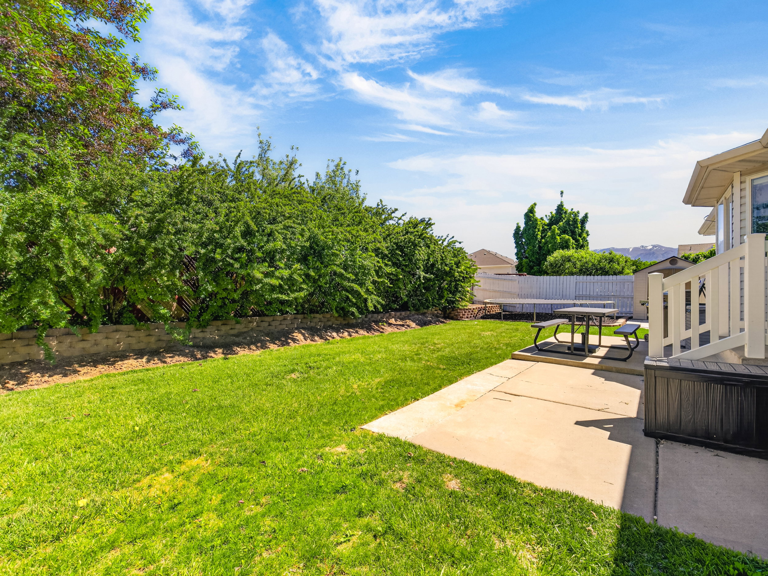 Expansive green lawn with mature perimeter shrubbery and a concrete patio