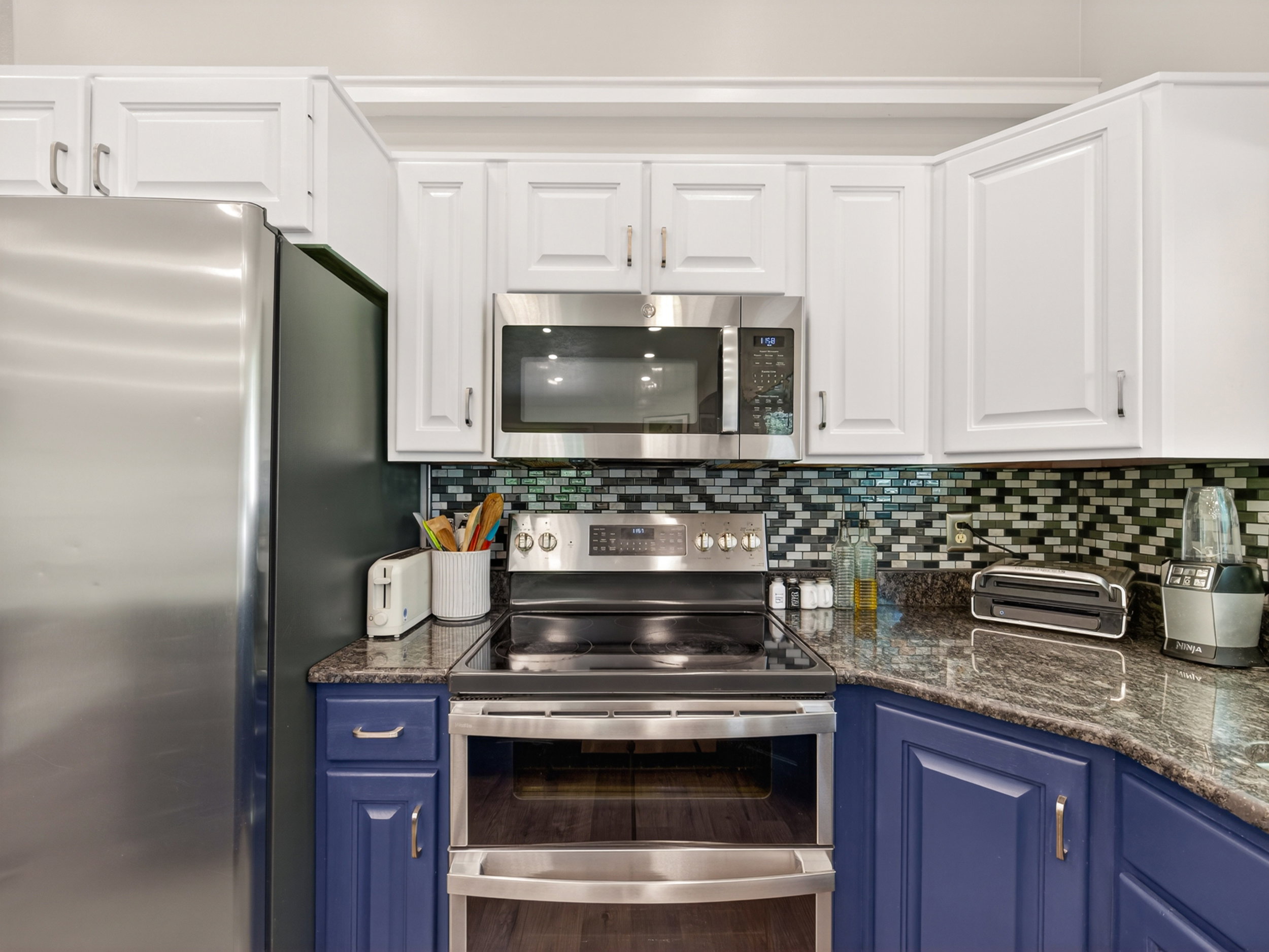 Kitchen featuring stainless steel appliances, white upper cabinetry, and blue lower cabinetry