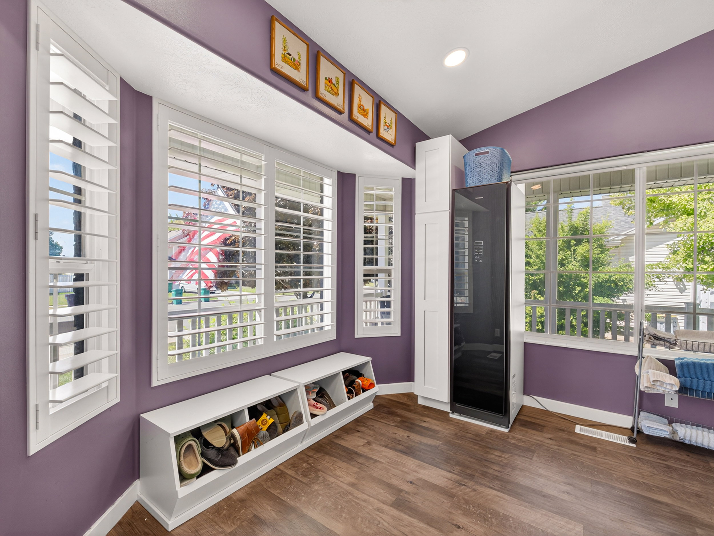 Spacious room featuring wood-finish flooring, white plantation shutters, and a large window bay