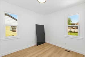 Bright room featuring wood-finish flooring, white walls, and two single-hung windows with white trim
