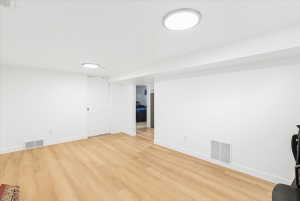 Spacious room featuring light wood-finish flooring, white walls, and recessed lighting fixtures