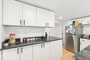 Kitchen featuring white shaker-style cabinetry, black hardware, dark stone countertops, and wood-finish flooring