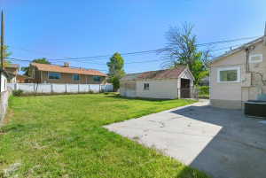 Expansive rear yard featuring a concrete pad, a detached storage building, and a chain-link fence