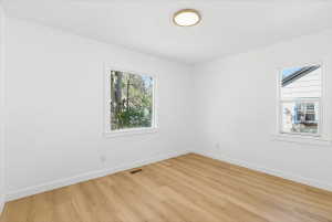 Light-filled interior featuring wood-finish flooring, crisp white walls, white baseboards, and a contemporary ceiling light fixture