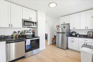 Kitchen featuring light wood-finish flooring, white cabinetry with black hardware, dark countertops, and stainless steel appliances
