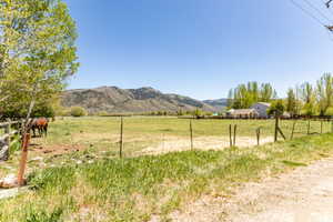 Expansive fenced pasture with distant mountainous terrain, mature deciduous trees, and a visible residential structure