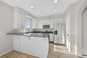 Kitchen featuring white cabinetry, stainless steel appliances, a bar-height counter, a window above the sink, and recessed lighting