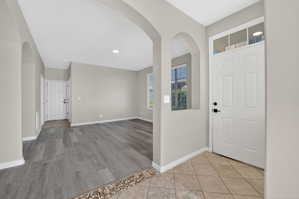 Entryway featuring light neutral wall tones, arched doorways, tile flooring, and a white paneled door with transom window