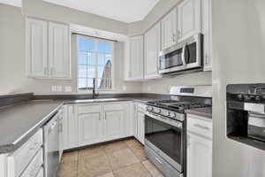 Kitchen featuring white cabinetry, dark countertops, a stainless steel gas range, a coordinating stainless steel microwave, and a window above the sink