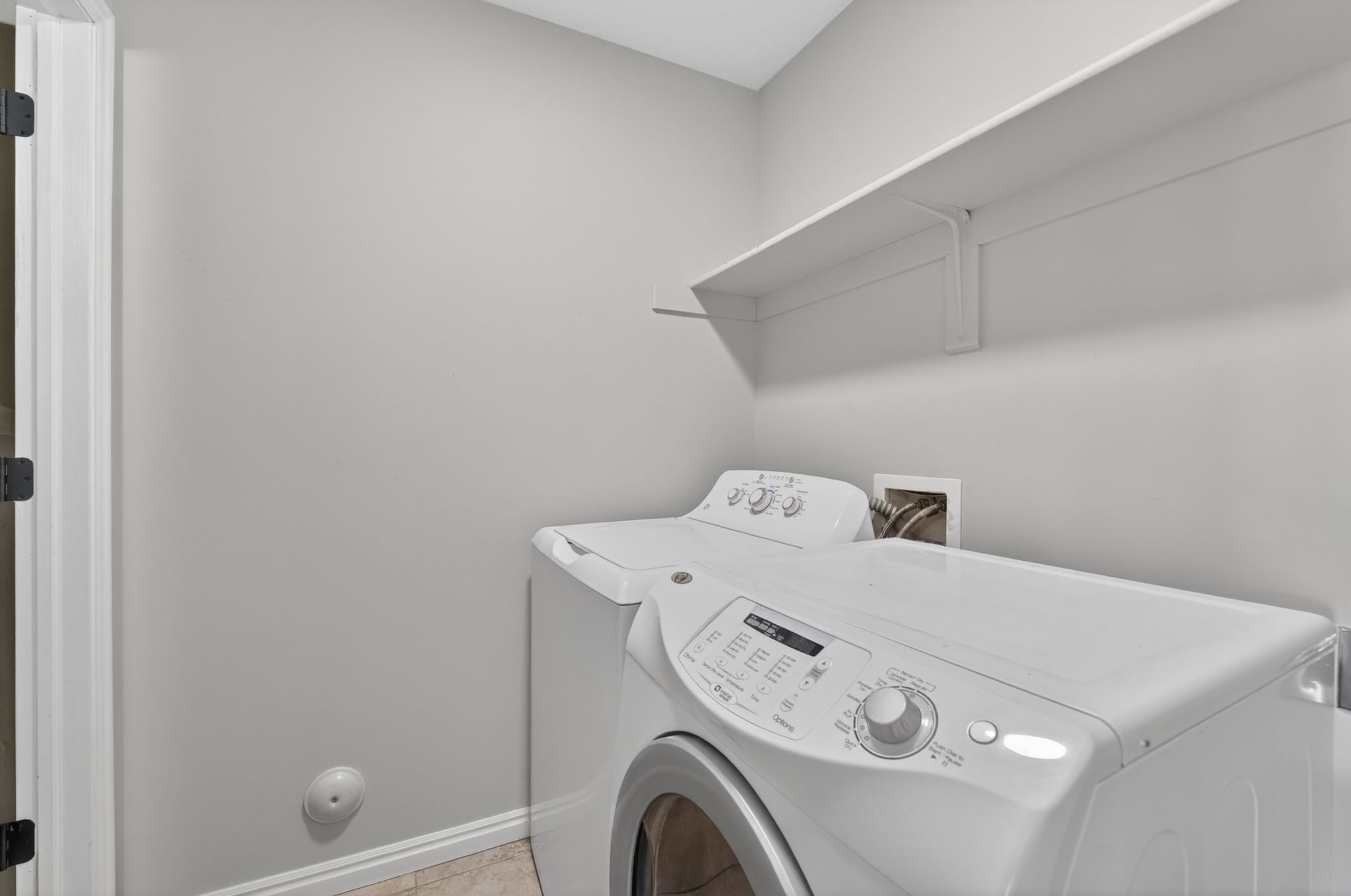 Dedicated laundry area featuring a white wall shelf, light gray wall paint, and white baseboards